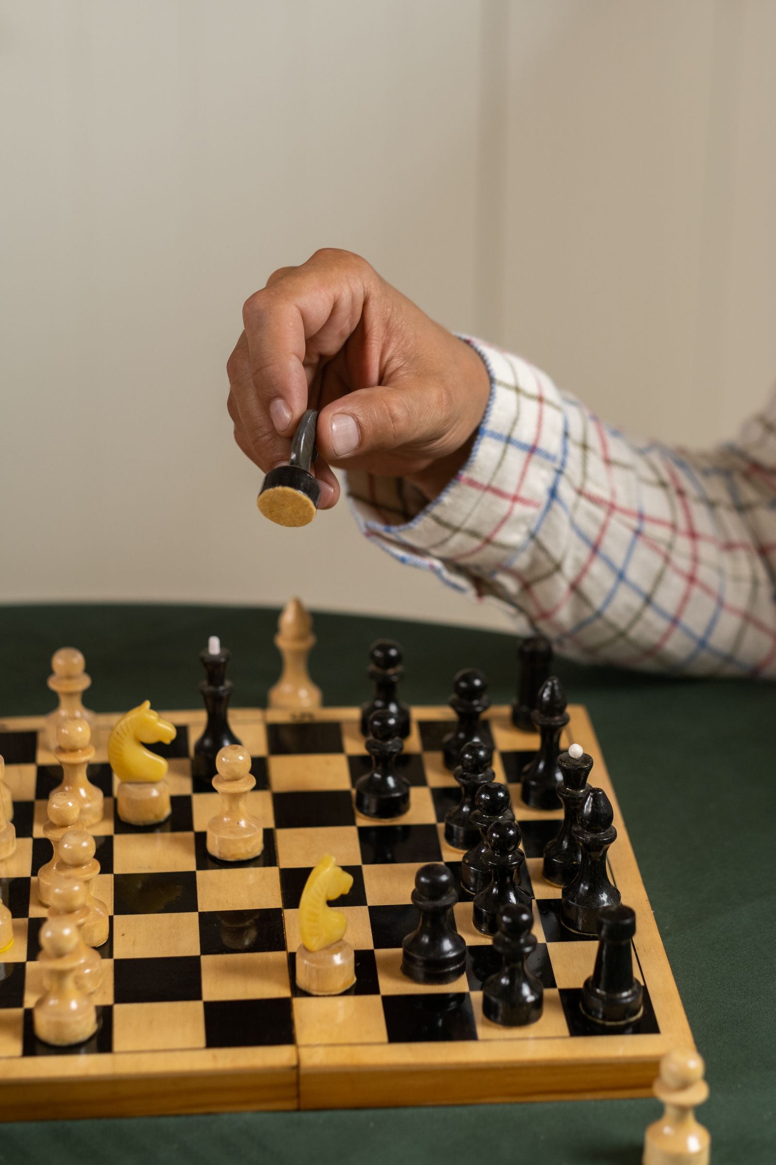 A hand holding a chess piece above a wooden board mid-move, illustrating the physical act of playing a move