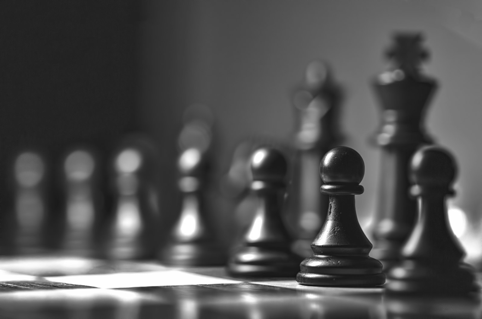 Close-up black and white photograph of chess pieces arranged on a board, pawns lined up in front of the king and queen