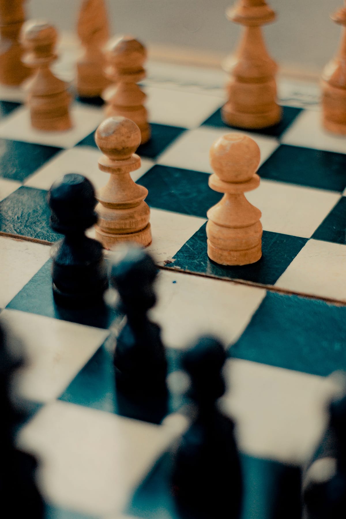 A white pawn and a black pawn standing on adjacent squares of a wooden chess board, facing each other